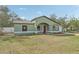 Exterior shot of a light green single-story house with a red door, lawn, and attached garage at 13083 Jaywalk Rd, Brooksville, FL 34614