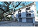 White building exterior with gray garage doors and a large oak tree at 6047 E Peppertree Way # 224, Sarasota, FL 34242