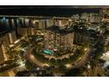 Night aerial view of a modern condo with a pool, trees, and city lights reflecting on the bay at 325 Golden Gate Pt # 802, Sarasota, FL 34236