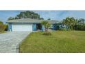 Charming blue home featuring a paved driveway, well-manicured lawn, lush tropical landscaping, and a white garage door at 429 N Rossetti Dr, Nokomis, FL 34275