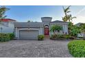 Beautiful home featuring manicured landscaping, a brick driveway, a two-car garage, and an elegant arched entryway at 3580 Fair Oaks Ln, Longboat Key, FL 34228