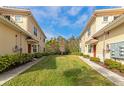 Well-manicured backyard area featuring green grass between tan townhomes under a blue sky at 8362 Enclave Way # 103, Sarasota, FL 34243