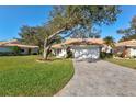 Charming single-story home with a tile roof, a manicured lawn, and a long brick driveway at 5718 Garden Lakes Palm, Bradenton, FL 34203