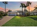 Exterior shot of home with well-manicured lawn, lush landscaping, and brick paved driveway at dusk at 6626 The Masters Ave, Lakewood Ranch, FL 34202