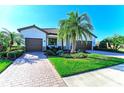 Inviting single-Gathering home featuring a lush front yard, brick driveway, and two-car garage at 324 Whispering Palms Ln, Bradenton, FL 34212