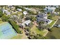 An aerial view of a waterfront property, surrounded by lush trees, a manicured lawn, and a nearby tennis court at 1621 Memory Ln, Sarasota, FL 34231