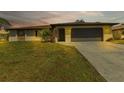 Single-story home with a brown roof, attached garage, and manicured lawn at dusk at 745 Columbia St, Port Charlotte, FL 33948