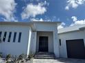 Close up of a modern white house with a metal roof, black front doors, stone stairs, and minimalist landscaping at 1426 Mineo Dr, Punta Gorda, FL 33950