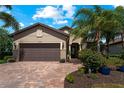 Beautiful home featuring a two-car garage, brick driveway, and manicured landscaping with tropical plants at 13948 Miranese St, Venice, FL 34293