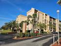 Beige condo building featuring manicured landscaping, palm trees, and clear blue skies at 3006 Caring Way # 409, Port Charlotte, FL 33952