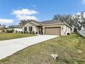 Beige home with a two-car garage, lush green lawn, white picket fence, and a spacious concrete driveway at 2822 Logsdon St, North Port, FL 34287