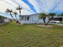 Front view of a white manufactured home with palm trees and a well-kept lawn at 8479 Tanaka Dr, Englewood, FL 34224