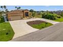 Tan house with brown roof and a long driveway, landscaping, and palm trees at 15204 Aquarius Cir, Port Charlotte, FL 33981
