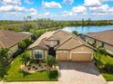 Stunning aerial view of a well-maintained home with a brick driveway, lush lawn, and a serene lake backdrop at 13587 Vancanza Dr, Venice, FL 34293