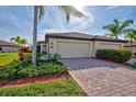 Two-car garage with a brick driveway and tropical landscaping at 20272 Tesoro Dr, Venice, FL 34293