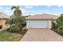 Tan villa with white garage door, landscaping, and paver driveway at 13364 Dimarco St, Venice, FL 34293