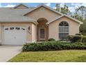Tan stucco home with white garage door, landscaping, and arched entryway at 826 Bayport Cir, Venice, FL 34292