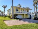 Inviting two-story yellow home with a white metal roof, covered balcony, and brick paver driveway at 1784 Bayshore Dr, Englewood, FL 34223