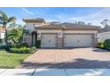 Charming home with a two-car garage, brick driveway, manicured lawn, and lush landscaping at 11903 Alessandro Ln, Venice, FL 34293