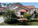 Well-maintained home featuring lush landscaping, a red tile roof, stucco siding, and a red awning at 4951 Summertree Rd, Venice, FL 34293