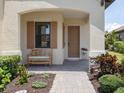 Inviting covered porch with a wooden bench, brick pavers, and colorful plants at 26825 Weiskopf Dr, Englewood, FL 34223