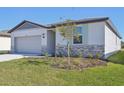 Single-story home with gray siding, stone accents, and a two-car garage. Landscaped yard at 7806 Gilchrist Springs Dr, Parrish, FL 34219