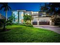 Striking two-story home featuring an arched entryway, manicured lawn, palm trees, and a two-car garage at dusk at 1100 Monterey Ne Blvd, St Petersburg, FL 33704