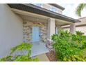 Front porch with stone wall, light blue door, and two white chairs at 14319 Italia Dr, Wimauma, FL 33598