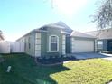 Green house with a two-car garage, landscaping, and a white fence at 8408 Canterbury Lake Blvd, Tampa, FL 33619
