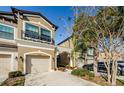 Tan three-story townhome with two-car garage, walkway, landscaping, and cars parked nearby at 11536 Crowned Sparrow Ln, Tampa, FL 33626