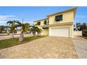 Two-story house with a yellow facade, white garage doors, and palm trees at 11325 5Th E St, Treasure Island, FL 33706