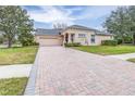 Brick driveway leading to a tan house with garage at 27325 Mistflower Dr, Wesley Chapel, FL 33544