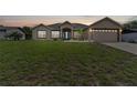 Tan house with blue door, attached garage, and large grassy yard at dusk at 4522 Gondolier Rd, Spring Hill, FL 34609