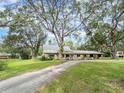 Single story home with a long driveway surrounded by lush greenery and large trees at 1080 Buena Vista Ave, Brooksville, FL 34601