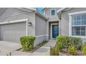 Gray house exterior with a dark blue front door, well-maintained landscaping, and a two-car garage at 10399 Gliding Eagle Way, Land O Lakes, FL 34638