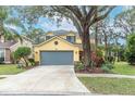 Two-story yellow house with gray garage door, landscaping, and a large tree in the front yard at 5608 Rockfield Loop, Valrico, FL 33596