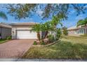 Charming home featuring a brick driveway, manicured lawn, tropical landscaping, and an attached two-car garage at 16127 Cape Coral Dr, Wimauma, FL 33598