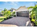 Dark brown two-car garage with paver driveway and tropical landscaping at 6137 Voyagers Pl, Apollo Beach, FL 33572