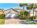 Single story home with a two-car garage, brick driveway and palm trees at 15724 Aurora Lake Cir, Wimauma, FL 33598