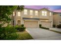 Dusk view of tan three-story townhome with two-car garage at 10108 Newel Valley Loop, Riverview, FL 33569