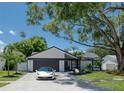 Mid-century home with white brick exterior, dark gray garage door, and lush landscaping at 14040 Cascade Ln, Tampa, FL 33618