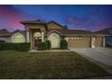 Evening view of tan house with three-car garage and landscaping at 10025 Cypress Shadow Ave, Tampa, FL 33647