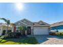 Tan house with red accents, a two-car garage, and lush landscaping at 14015 Kingfisher Glen Dr, Lithia, FL 33547