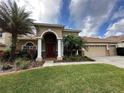 Tan house with a red door, three-car garage, and lush landscaping at 3011 Marble Crest Dr, Land O Lakes, FL 34638