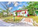 A quaint single-story home featuring a charming red-trimmed porch, surrounded by lush greenery and a tidy front yard at 5308 Ben Hur Dr, St Petersburg, FL 33708