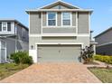 Close-up of a two-story home featuring gray siding, a brick driveway, and mature landscaping at 11616 Little River Way, Parrish, FL 34219