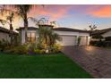 Stunning single-story home with a three-car garage, brick driveway, and mature tropical landscaping at sunset at 706 Acacia Ct, Bradenton, FL 34212