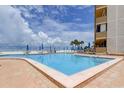 An inviting community pool with lounge chairs and umbrellas under a blue sky with fluffy white clouds at 5396 Gulf Blvd # 110, St Pete Beach, FL 33706