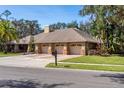 Street-level view of three-car garage home featuring lush landscaping, neutral paint, brick accents and a basketball hoop at 70 Deerpath Dr, Oldsmar, FL 34677