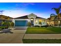 Twilight view of a charming single-story home featuring a manicured lawn, and a striking blue garage door at 14445 Haddon Mist Dr, Wimauma, FL 33598